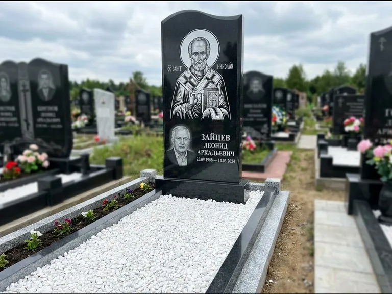 Памятник с гравировкой иконы: стела с крестообразным навершием — икона в резной рамке-киоте, газон без ограды, стриженая трава, работа «Раевская» в Южно-Сахалинске