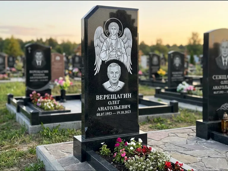 Памятник с гравировкой иконы: стела с резным навершием и нимбом в золоте — гравировка образа Спасителя, высокие разросшиеся туи полукругом, работа «Мельникова» в Южно-Сахалинске