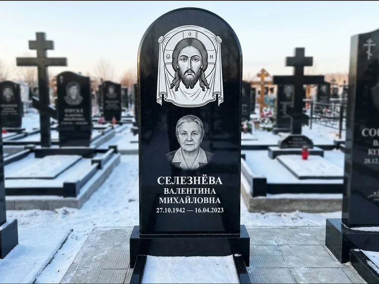 Памятник с гравировкой иконы: небольшая скромная одиночная стела с именной иконой — золочёный нимб на образе, аккуратный участок с газоном, работа «Ковалёв» в Южно-Сахалинске