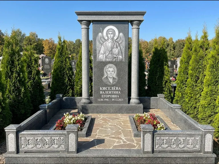 Памятник с гравировкой иконы: массивная стела с двускатным навершием-домиком — гравировка Николая Чудотворца, живая изгородь из туи, работа «Журавлёв» в Южно-Сахалинске