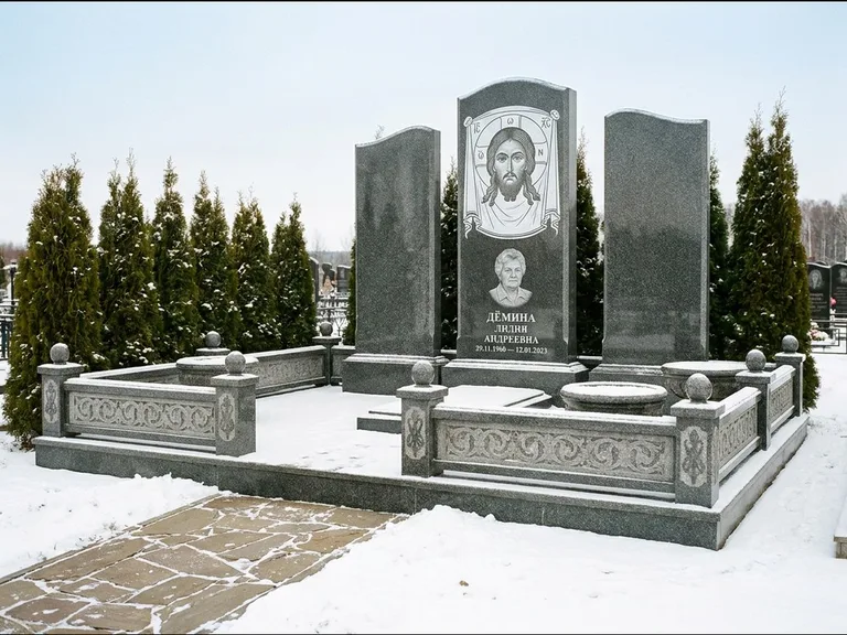 Памятник с гравировкой иконы: узкая вертикальная стела-пилон с ликом — икона в резной рамке-киоте, открытая лужайка без ограды, работа «Одинцов» в Южно-Сахалинске