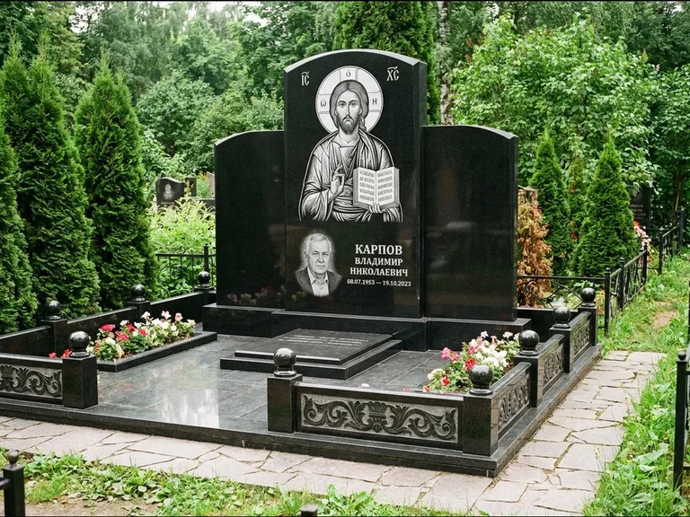 Памятник с гравировкой иконы: широкая панорамная стела с золочёным нимбом — гравировка образа Матроны Московской, цветник с белыми хризантемами, работа «Мельникова» в Южно-Сахалинске