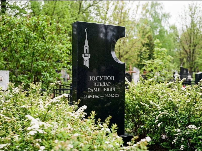 Мусульманский памятник с гравировкой мечети: стела с боковым вырезом в форме полумесяца — гравировка минарета с полумесяцем, низкие кусты спиреи в цвету, работа «Юсупов» в Южно-Сахалинске